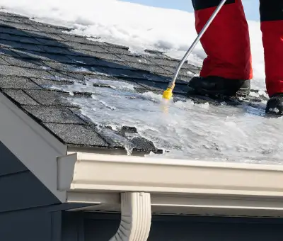 Ice dam removal technician using a steam wand to melt thick ice buildup on a residential roof in Louisville, KY