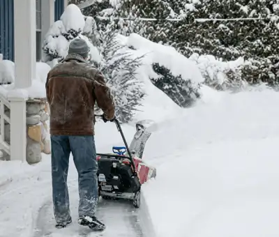Residential snow removal technician using a snow blower to clear a home driveway and walkway in Louisville, KY