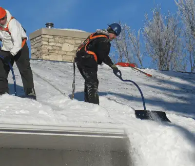 Professional technicians performing roof snow removal with safety harnesses and shovels in Louisville, KY